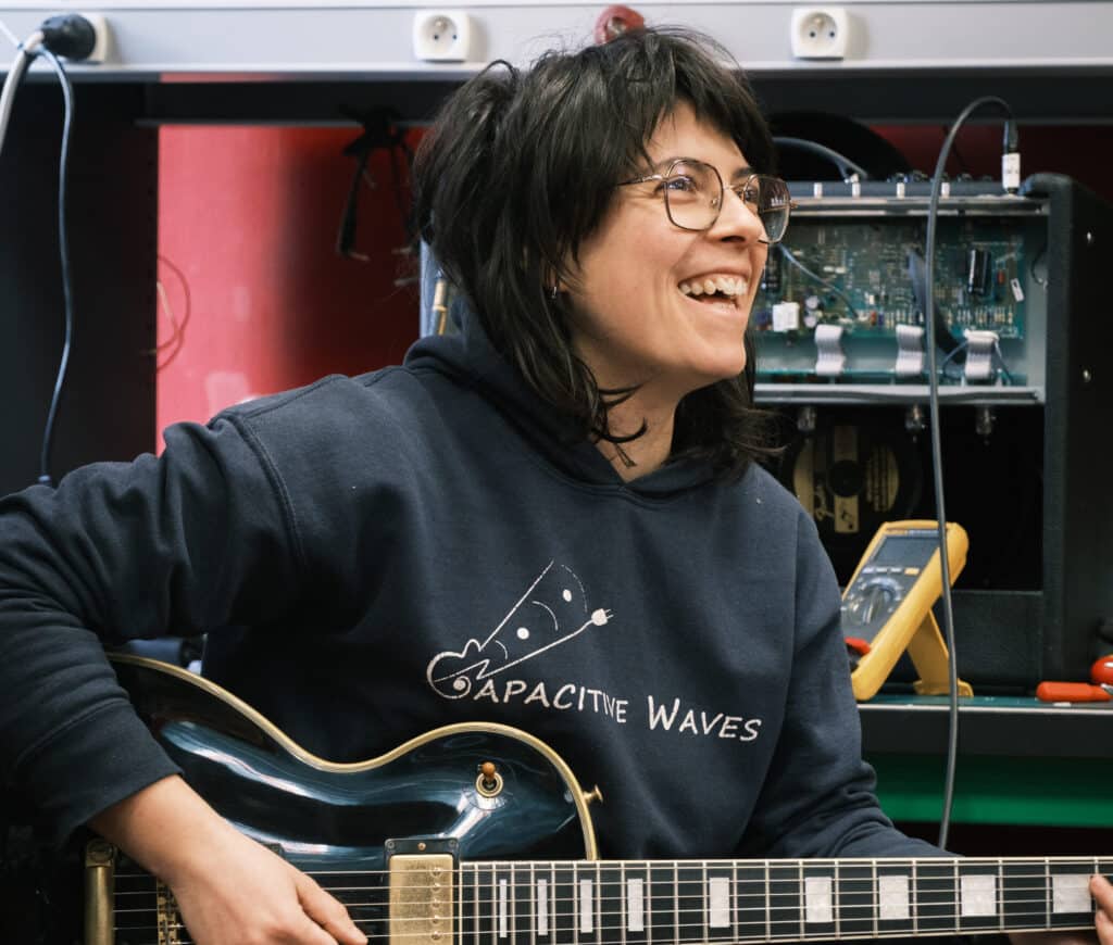 Sarah joue d’une guitare électrique devant un ampli ouvert dans l’atelier Capacitive Waves
